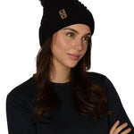 Female model wearing the Diamond Knit Pom Beanie in black, showcasing the faux fur pom and leather logo tab.