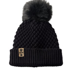 Product flat lay of the Diamond Knit Pom Beanie in black, displaying the ribbed cuff, diamond knit design, and leather logo tab with faux fur pom.