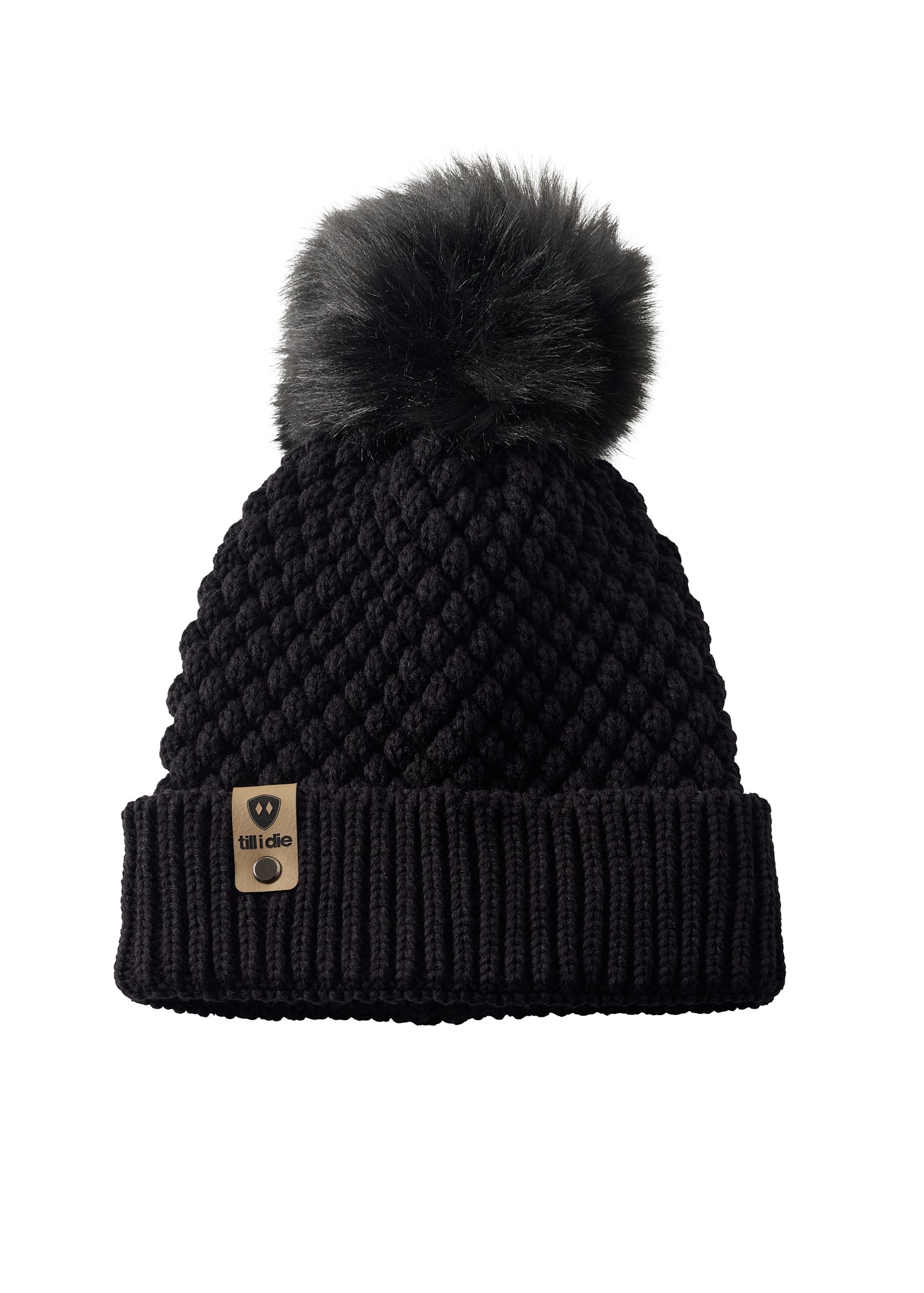 Product flat lay of the Diamond Knit Pom Beanie in black, displaying the ribbed cuff, diamond knit design, and leather logo tab with faux fur pom.