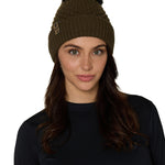 Female model wearing the Diamond Knit Pom Beanie in military olive, showcasing the faux fur pom and leather logo tab.