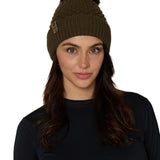 Female model wearing the Diamond Knit Pom Beanie in military olive, showcasing the faux fur pom and leather logo tab.