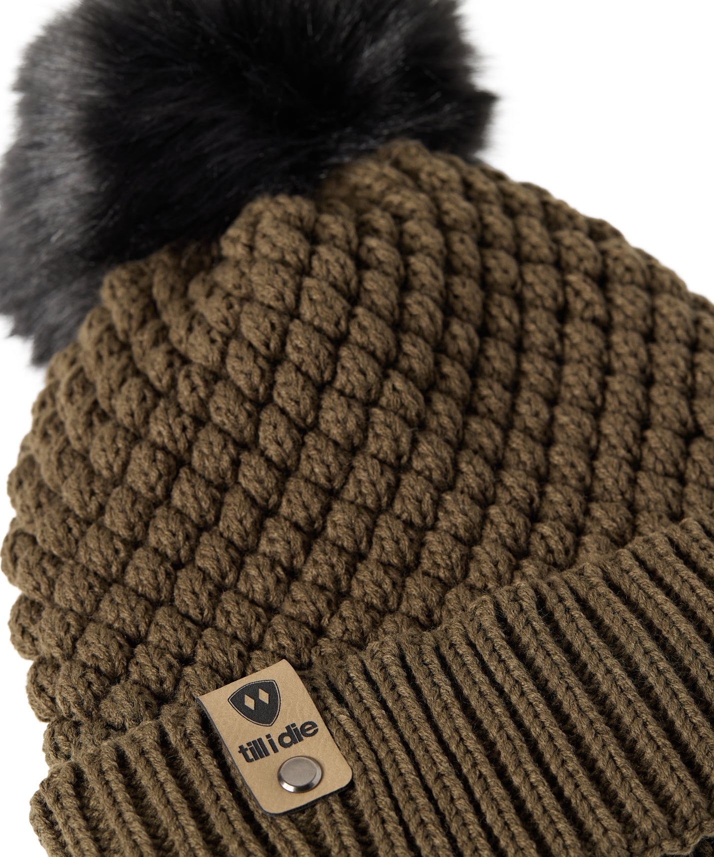 Close-up flat lay of the Diamond Knit Pom Beanie showing the textured diamond knit pattern, faux fur pom, and logo leather tab.