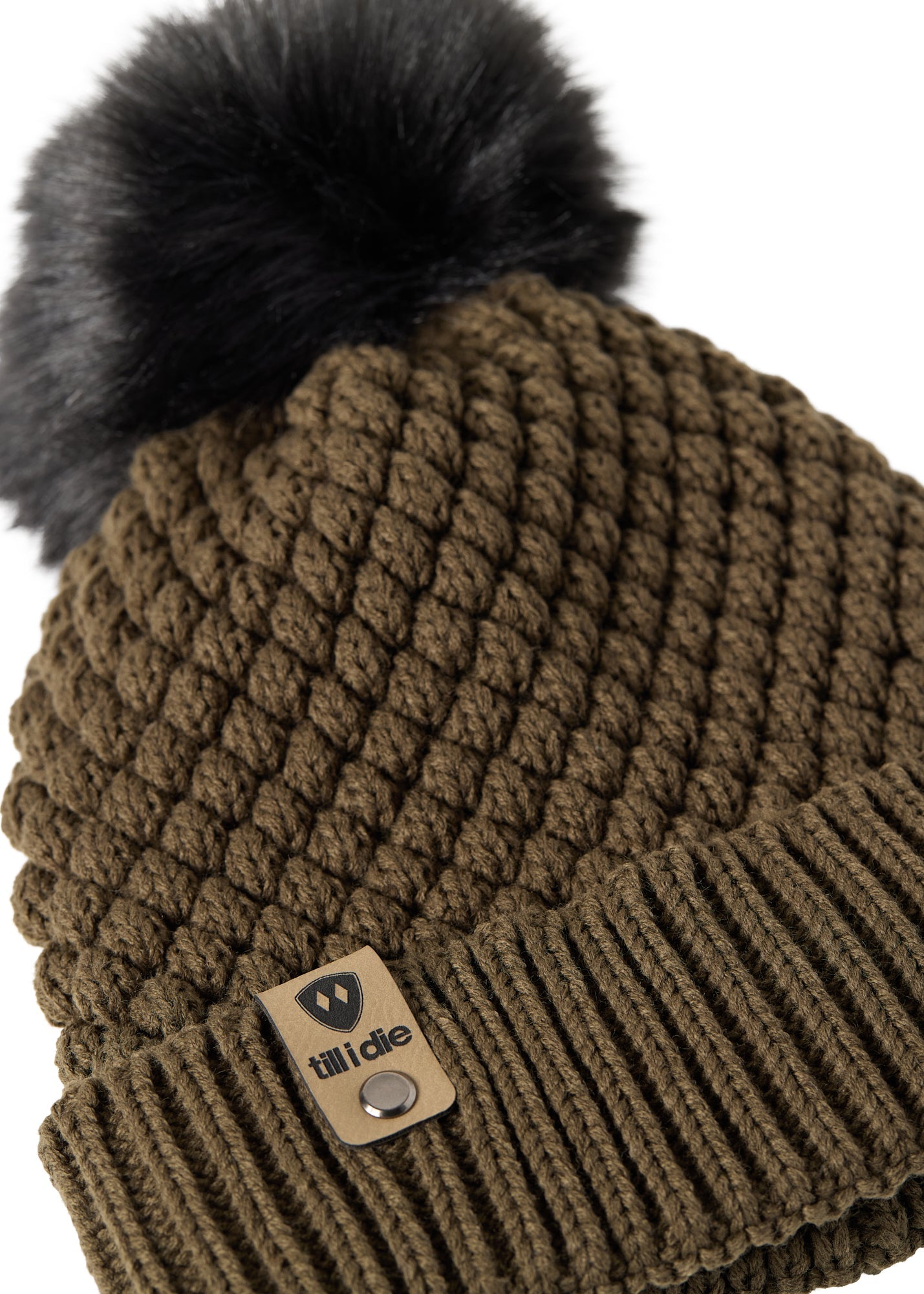 Close-up flat lay of the Diamond Knit Pom Beanie showing the textured diamond knit pattern, faux fur pom, and logo leather tab.