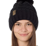 Front view of a female model wearing the black knit pom beanie hat in black on a white background. the hat features a matching pom pom, leather tab with embossed black till i die logo and nickel fastener. 