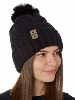 Side view of a female model wearing the black knit pom beanie hat in black on a white background. the hat features a matching pom pom, leather tab with embossed black till i die logo and nickel fastener. 