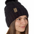 Side view of a female model wearing the black knit pom beanie hat in black on a white background. the hat features a matching pom pom, leather tab with embossed black till i die logo and nickel fastener. 