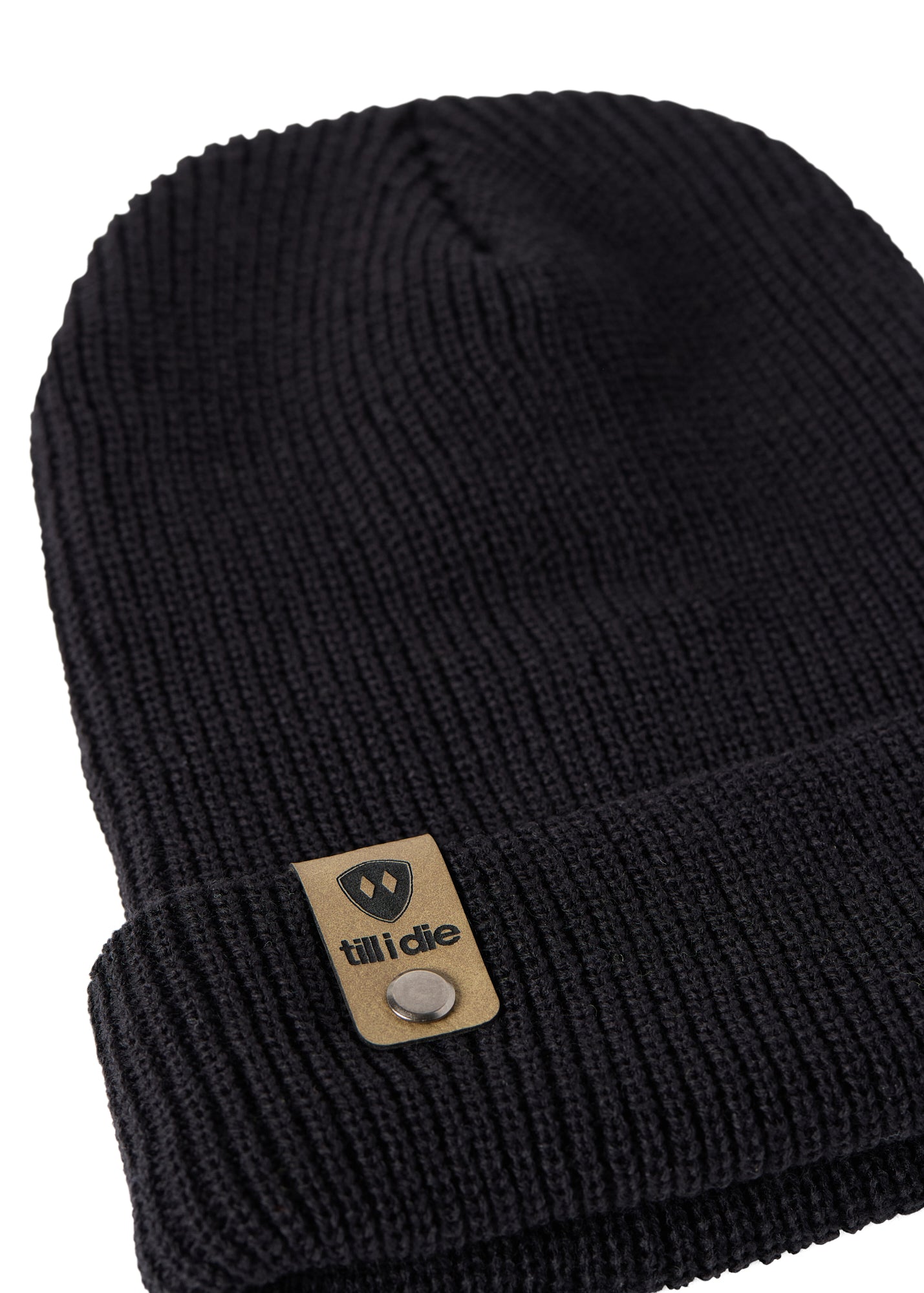 Flat lay of the Till I Die black knit beanie showing close-up detail of the medium gauge knit and branded leather logo tab on the cuff