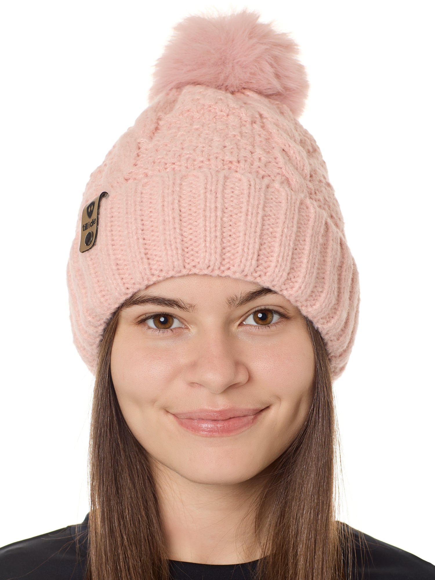 front view of a female model wearing a blush knit pom beanie featuring a matching pom pom, cuff and leather till i die logo tab with a nickel fastener.