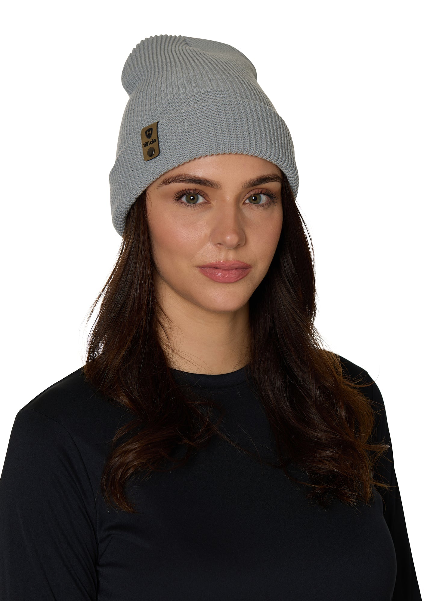 Female model wearing the Till I Die Leather Tab Knit Beanie in cadet blue, styled with the cuff folded to show the branded leather logo tab