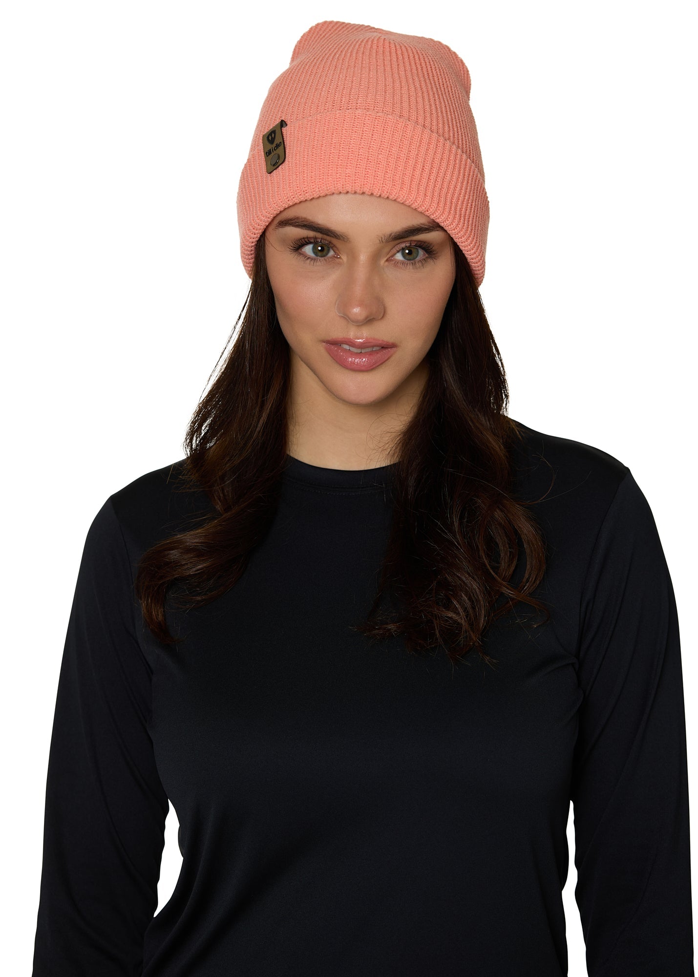 Female model wearing the Till I Die Leather Tab Knit Beanie in coral, styled with the cuff folded to show the branded leather logo tab