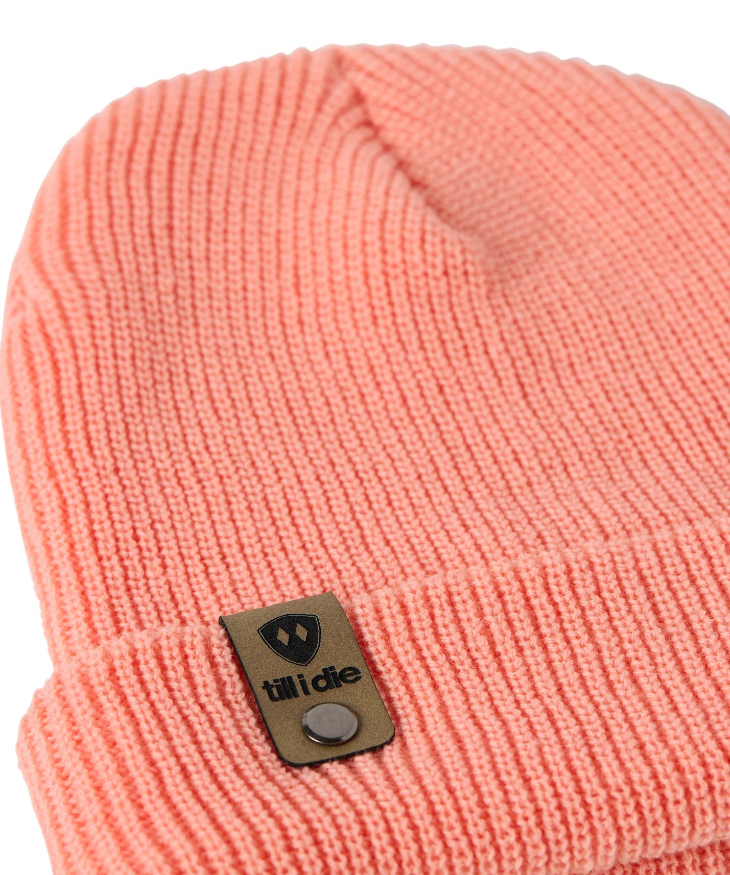 Flat lay of the Till I Die coral  knit beanie showing close-up detail of the medium gauge knit and branded leather logo tab on the cuff
