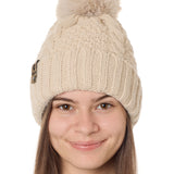 front view of a female model wearing a vintage white knit pom beanie featuring a matching pom pom, cuff and leather till i die logo tab with a nickel fastener.