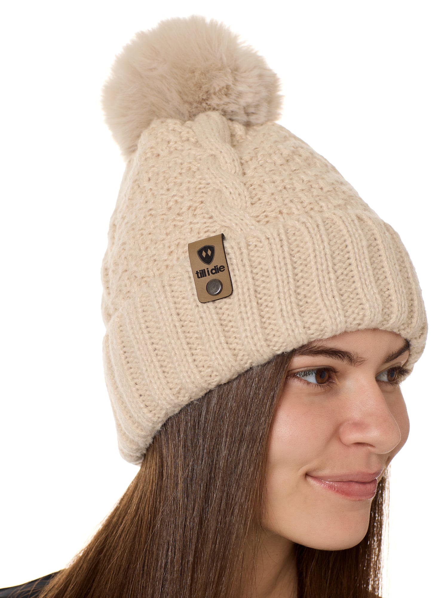 side view of a female model wearing a vintage white knit pom beanie featuring a matching pom pom, cuff and leather till i die logo tab with a nickel fastener.