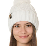 front view of a female model wearing a white knit pom beanie featuring a matching pom pom, cuff and leather till i die logo tab with a nickel fastener.