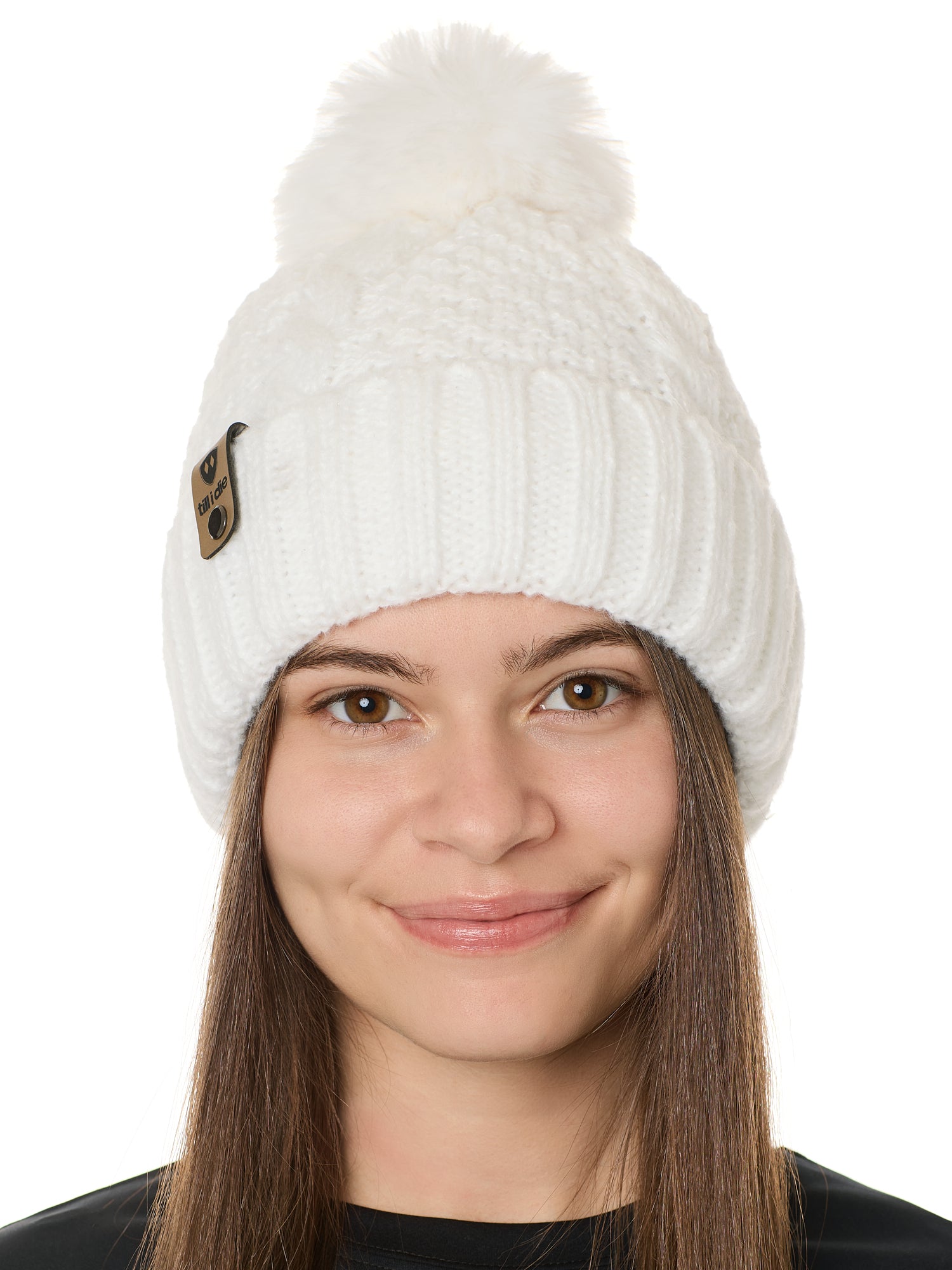 front view of a female model wearing a white knit pom beanie featuring a matching pom pom, cuff and leather till i die logo tab with a nickel fastener.