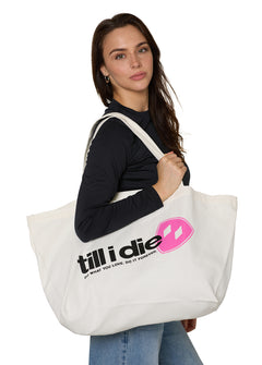 female model carrying a natural canvas tote with till i die text, pink shield, and "do what you love. do it forever."