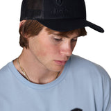 Male model wearing the Till I Die Black-on-Black Trucker Hat, showing the front puff embroidered logo and mesh back.