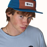 Person wearing a blue and brown cap with Tillidie logo, looking to the side.