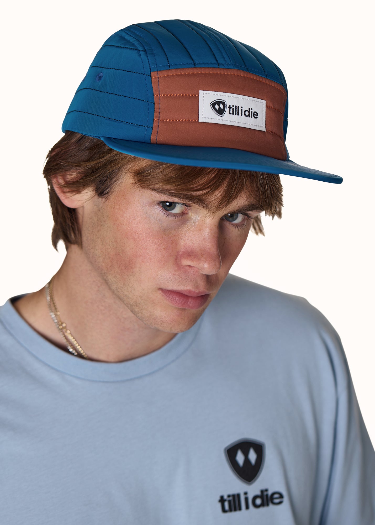 Person wearing a blue and brown cap with Tillidie logo, looking to the side.