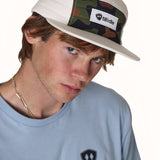 male model wearing a white quilted camp hat with a till i die woven label on the front. The hat also has a classic camo front panel and white brim.