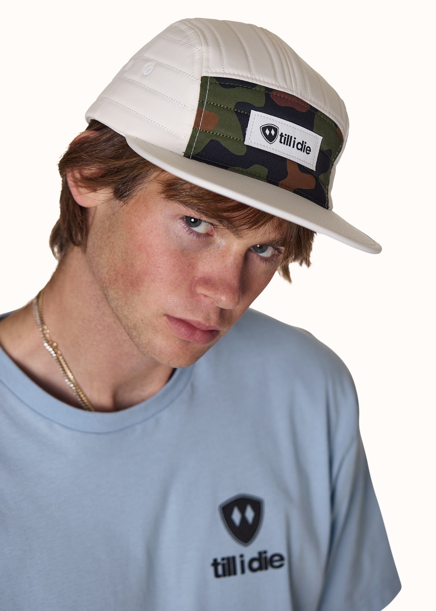 male model wearing a white quilted camp hat with a till i die woven label on the front. The hat also has a classic camo front panel and white brim.