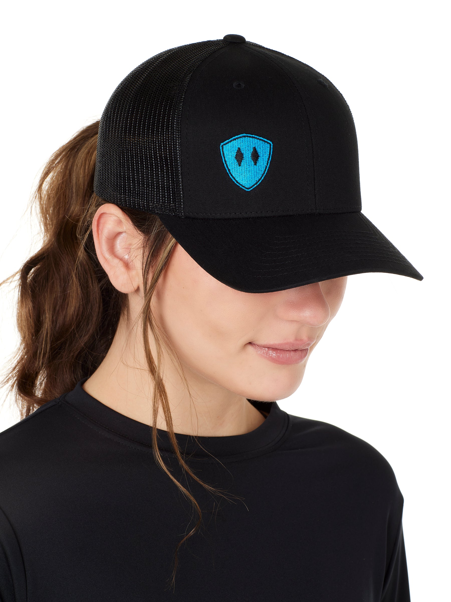Front view of a female wearing a black classic trucker hat with a blue embroidered double diamond shield on the bottom right panel