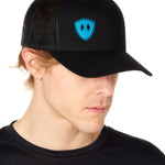 Front view of a male wearing a black classic trucker hat with a blue embroidered double diamond shield on the bottom right panel