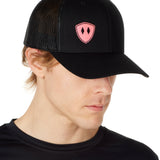 Front view of a male wearing a black classic trucker hat with a pink embroidered double diamond shield on the bottom right panel
