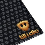 Close-up flat lay showing the gold Till I Die logo printed near the bottom right hem of the neck gaiter.