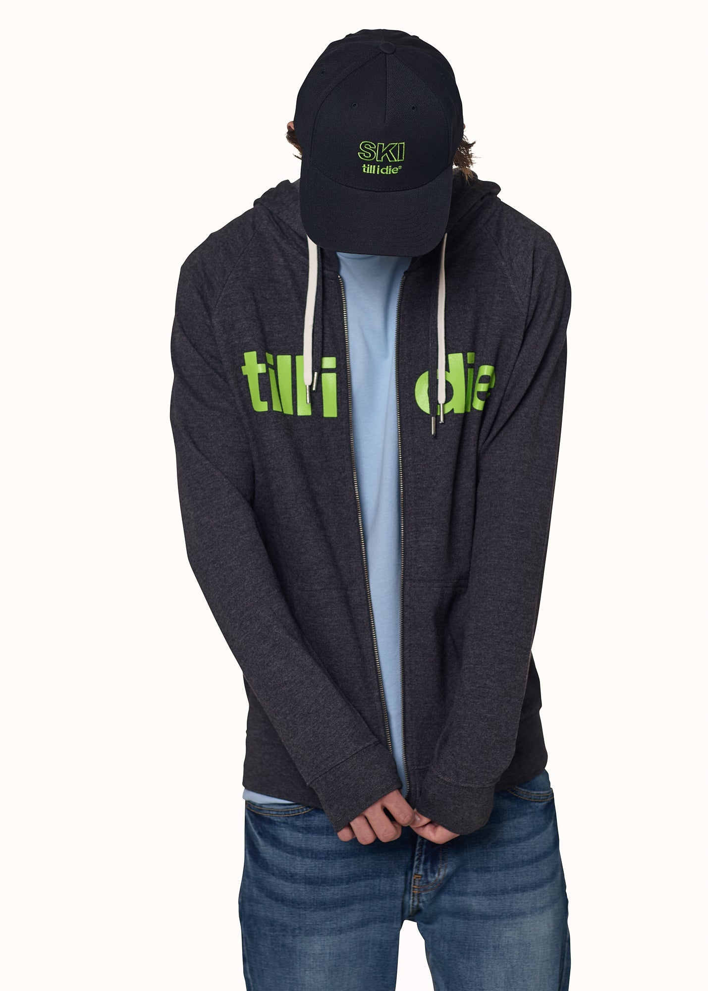 Male model in full Till I Die outfit featuring Ski Till I Die hat and zip hoodie with green logo