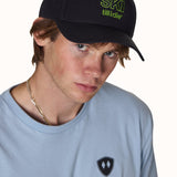 Male model wearing Ski Till I Die embroidered hat in black with neon green logo and curved bill