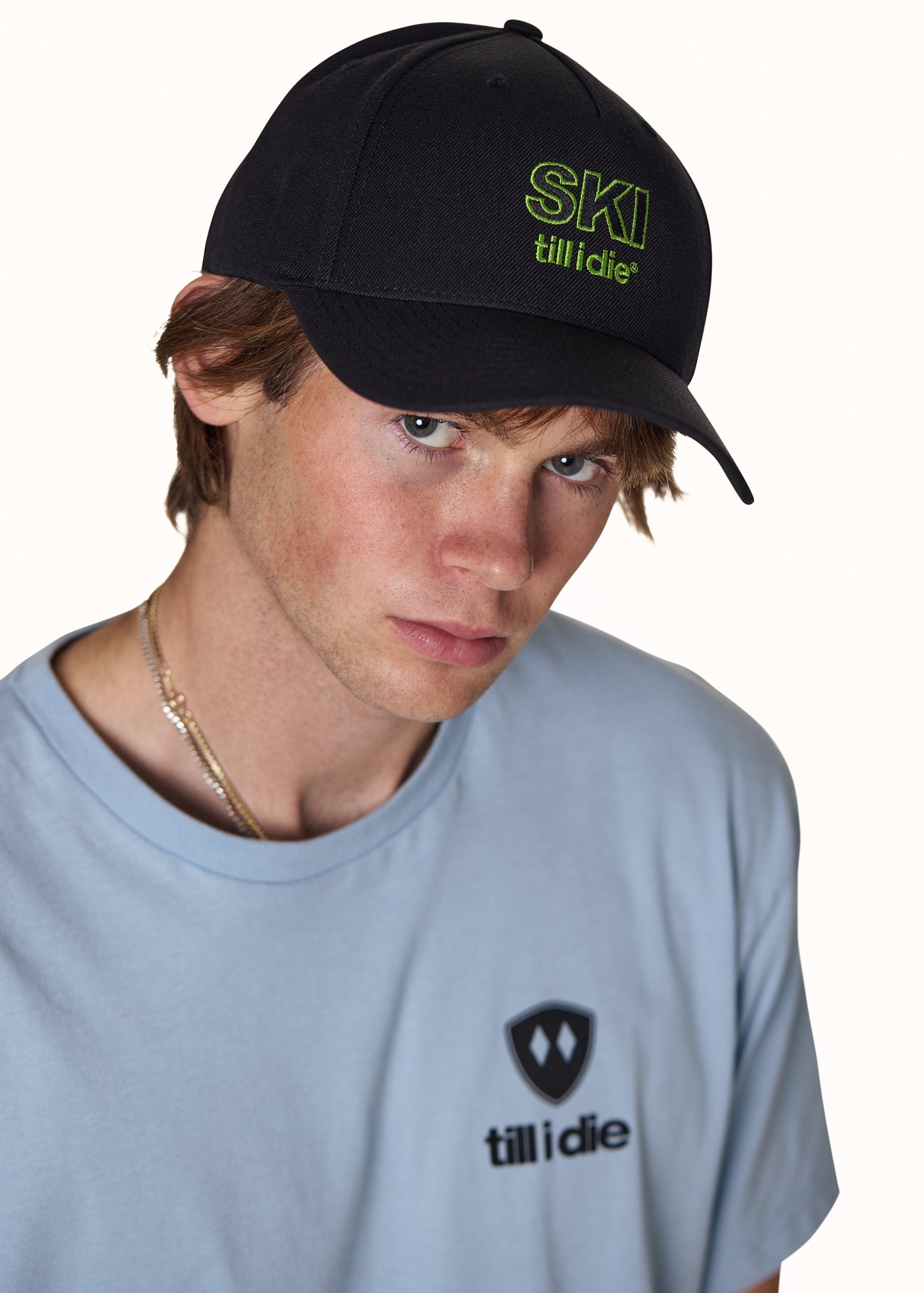 Male model wearing Ski Till I Die embroidered hat in black with neon green logo and curved bill