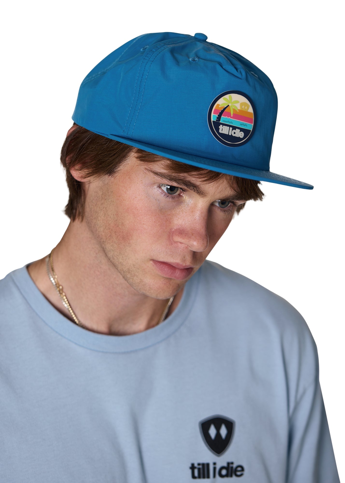 model wearing the marine blue sunset session surf hat, the hat has a pvc round patch with a palm tree and sunset graphic with the word "till i die"
