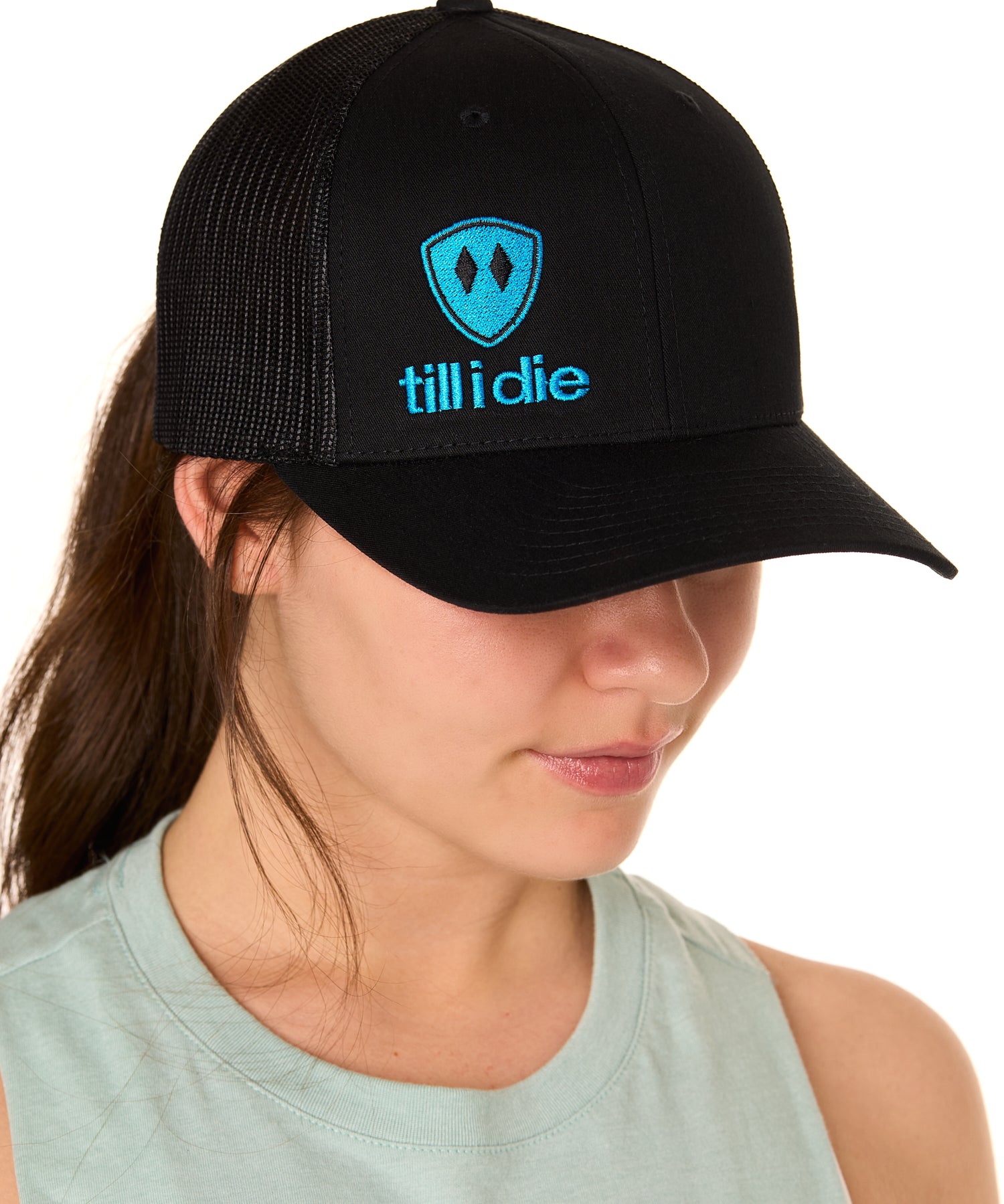 Front view of a female model wearing a black classic trucker hat, featuring a blue embroidered Till I Die logo on the lower right front panel.