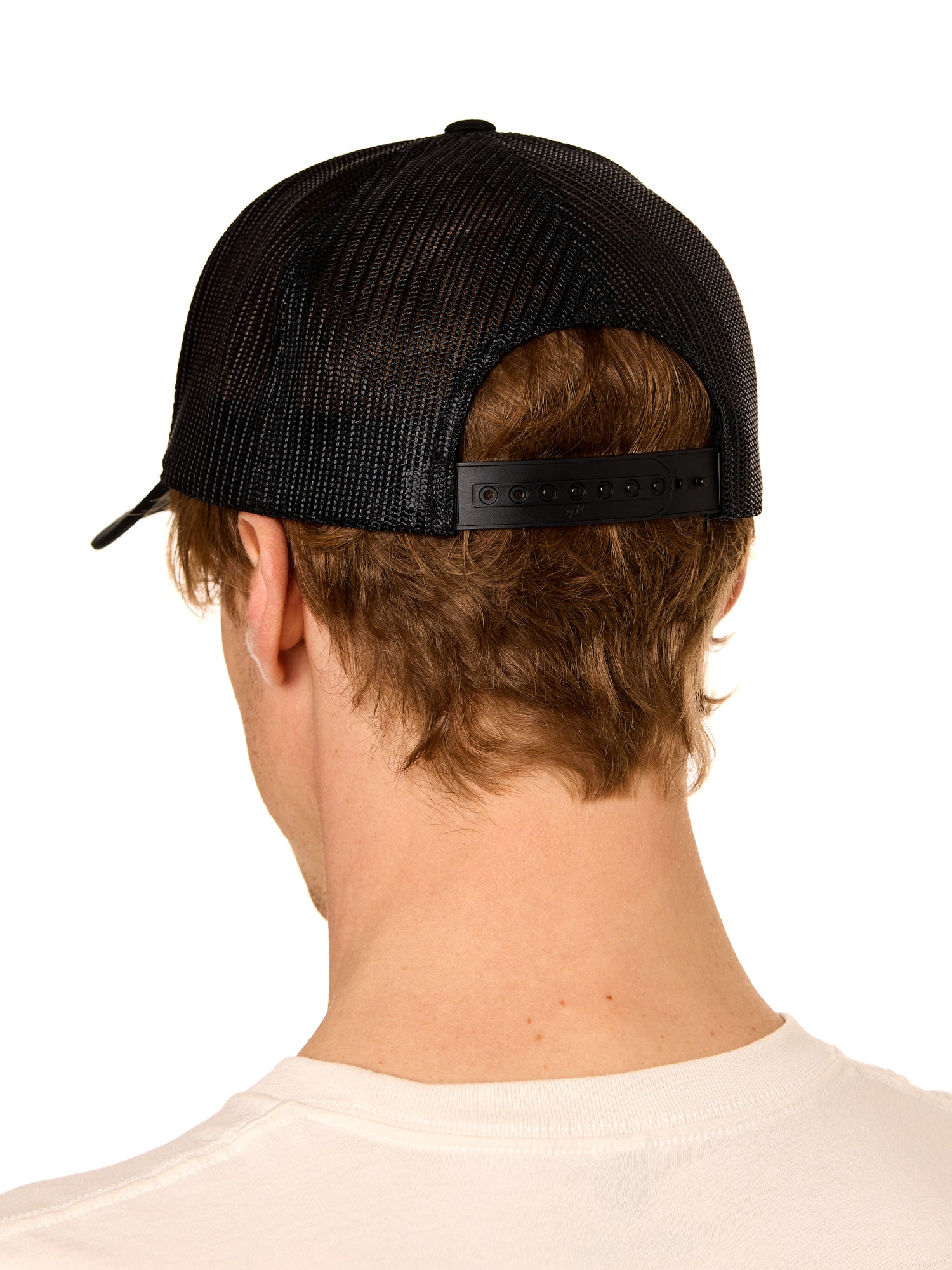 Back view of a male model wearing a classic black trucker hat featuring the mesh back panels and matching black snapback closure