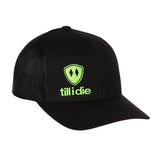 Front view of a black classic trucker hat, featuring a green embroidered Till I Die logo with double black diamonds and a green shield on the lower right front panel on a white background.