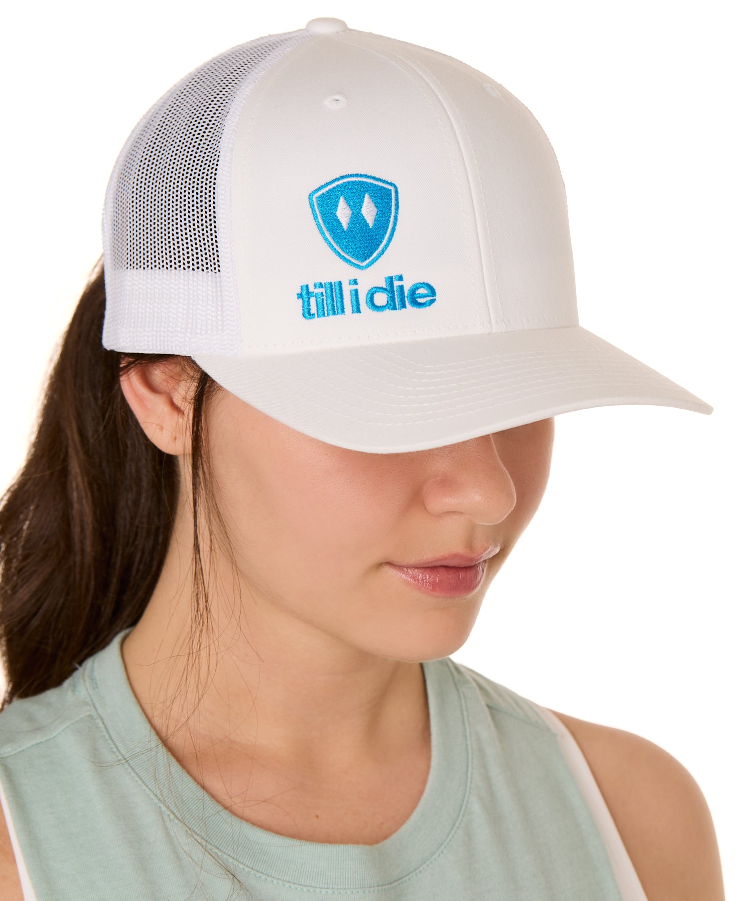 Front view of a female model wearing a white classic trucker hat, featuring a blue embroidered Till I Die logo on the lower right front panel.