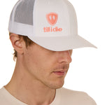 Front view of a male model wearing a white classic trucker hat, featuring a coral embroidered Till I Die logo on the lower right front panel.