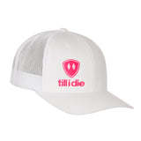 Front view of a white classic trucker hat, featuring a hot pink embroidered Till I Die logo with double white diamonds and a hot pink shield on the lower right front panel on a white background.
