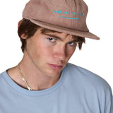 Model wearing the Wet and Wrecked corduroy surf hat in dusty rose, the hat has bright teal embroidery of a surfboard with word 'Wet and Wrecked' 