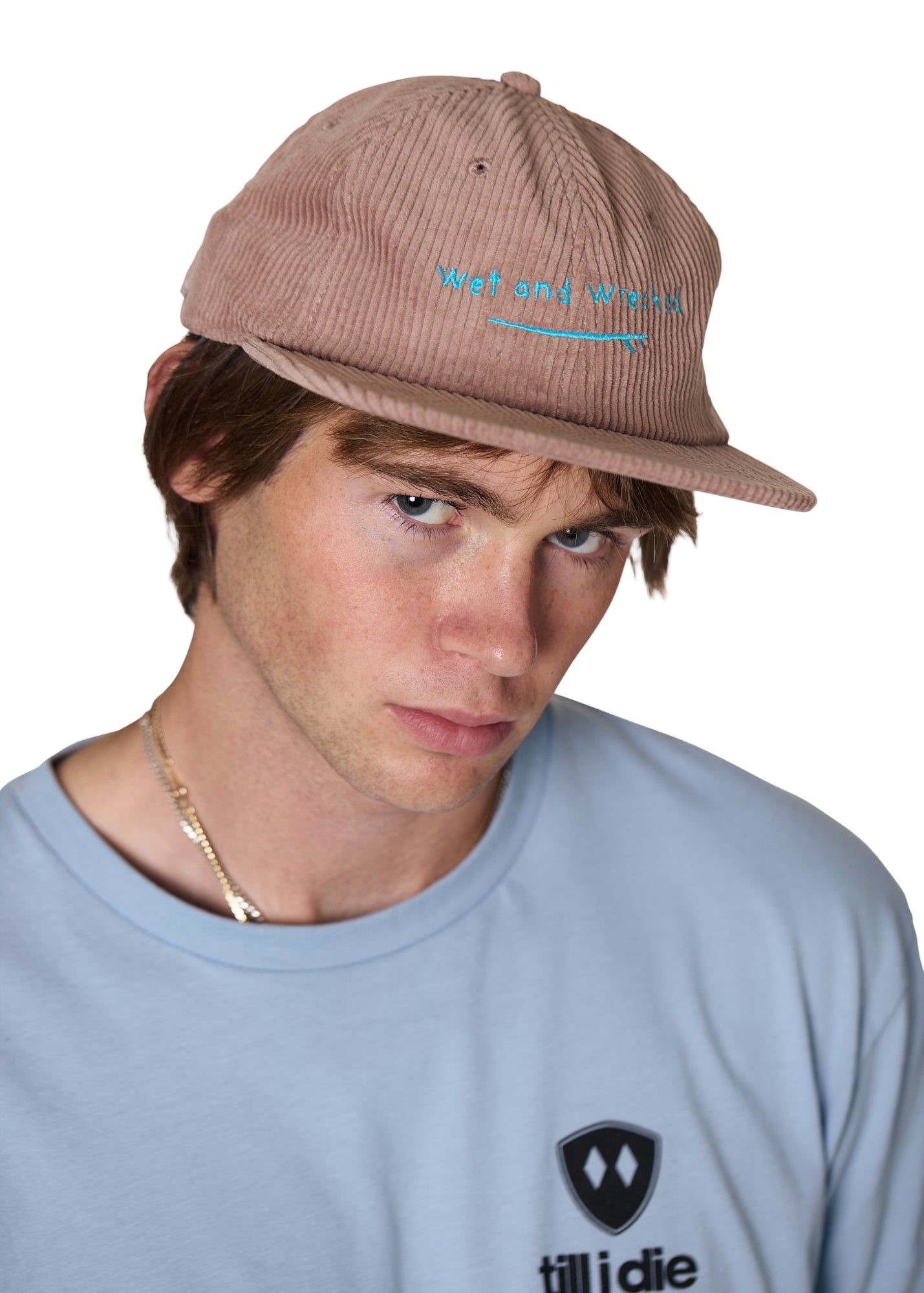 Model wearing the Wet and Wrecked corduroy surf hat in dusty rose, the hat has bright teal embroidery of a surfboard with word 'Wet and Wrecked' 