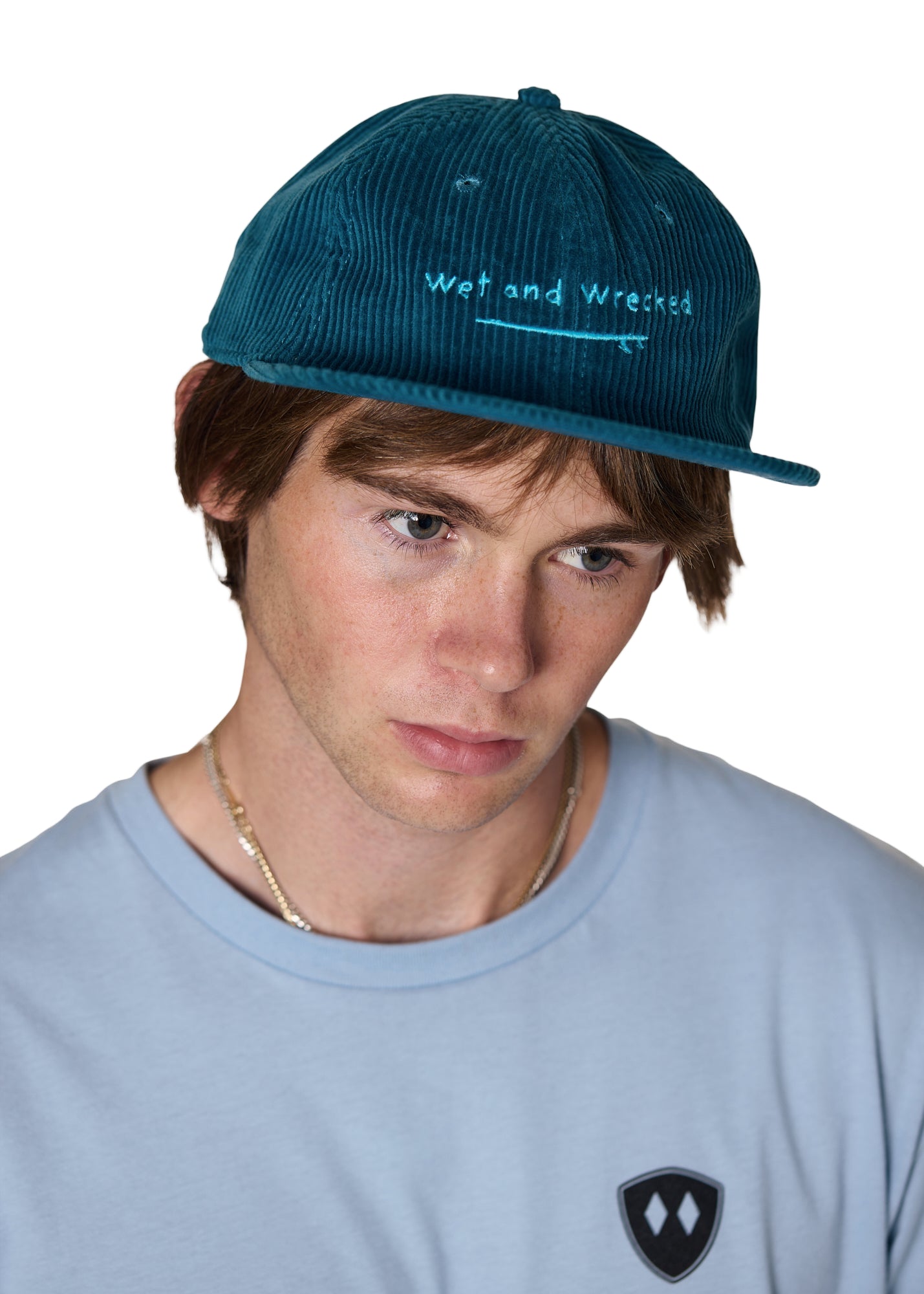 model wearing the corduroy surf hat in teal, has has light teal embroidery of a surf board and the words 'wet and wrecked'