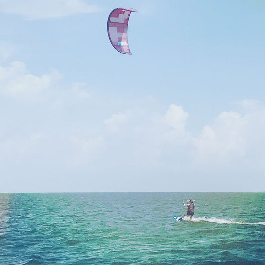 Person kiteboarding on a clear day with a colorful kite above the water.
