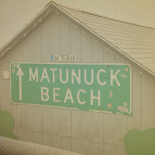 Green sign pointing to Matunuck Beach in front of a wooden building.