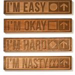 Collection of four cherry wood-carved ski trail signs displayed on a white background. Each sign features a different trail difficulty: “I’m Easy” with a green circle, “I’m Okay” with a blue square, “I’m Hard” with a black diamond, and “I’m Nasty” with double black diamonds—each paired with an upward-pointing arrow.