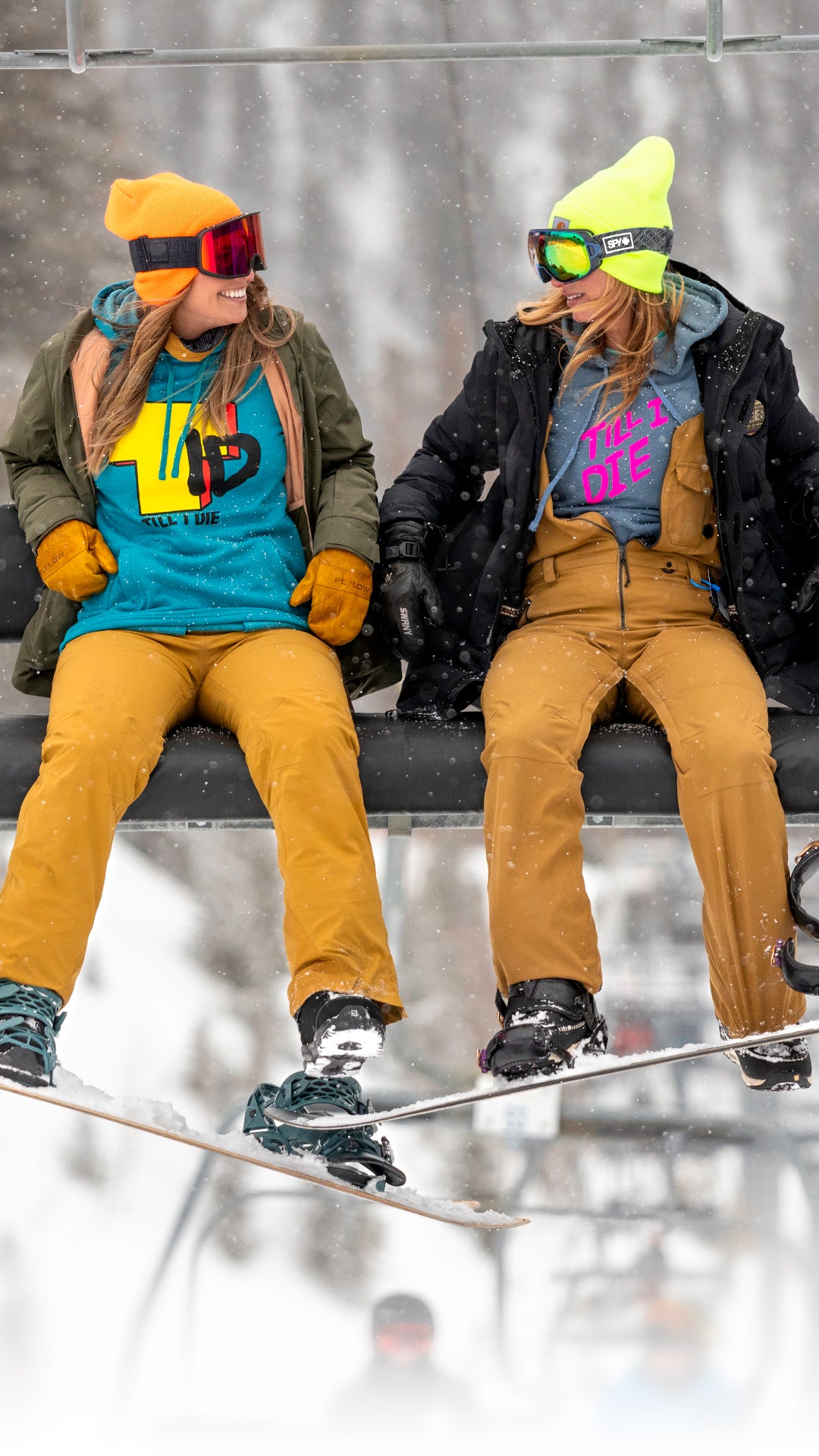 Two girls sitting on a chairlift wearing Till I Die hoodies
